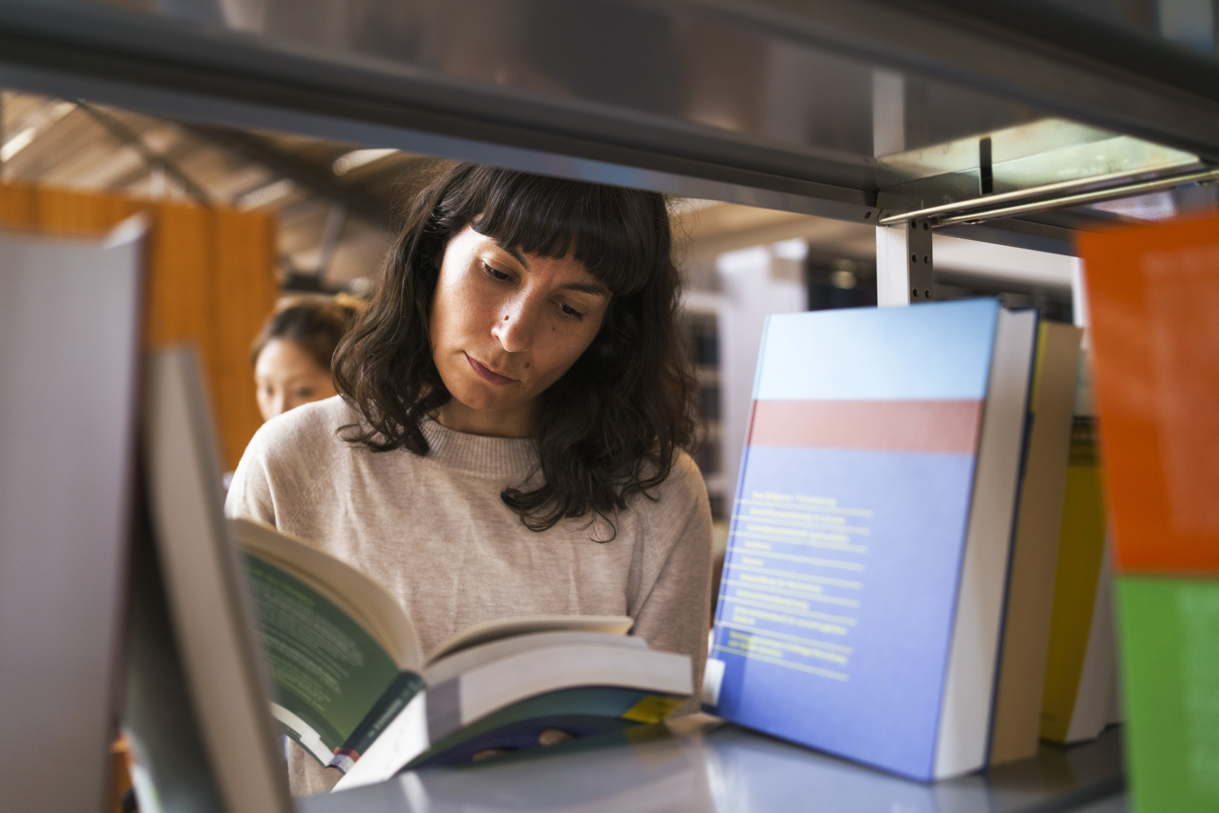 En kvinna läser en bok i ett bibliotek.