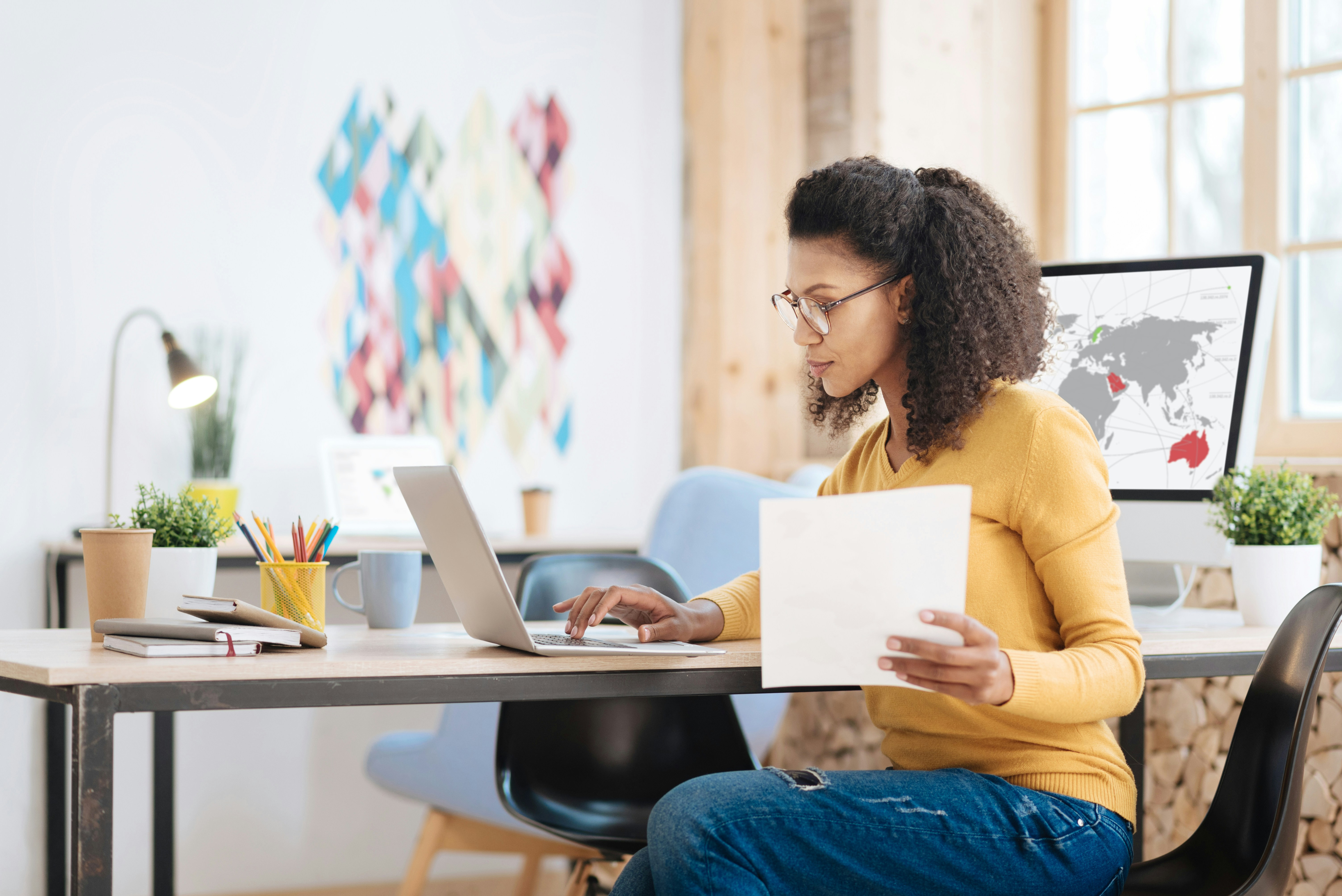En kvinna sitter vid ett bord med en bärbar dator och papper.