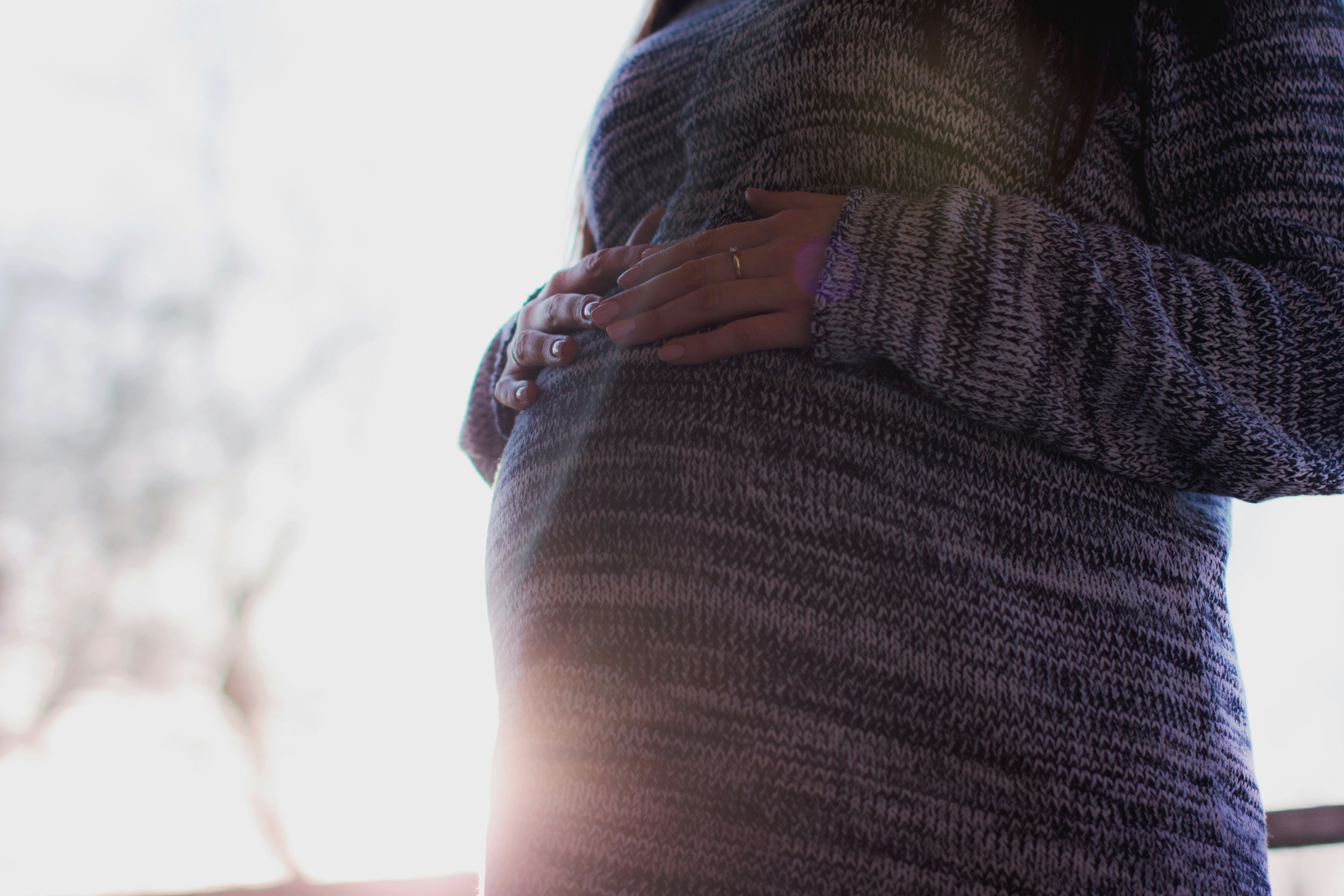 En gravid kvinna som står med händerna på magen.