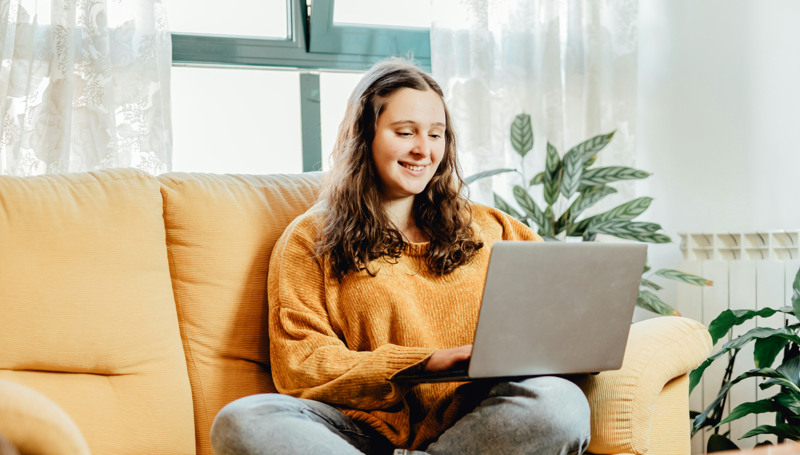 En kvinna sitter i en soffa med en bärbar dator