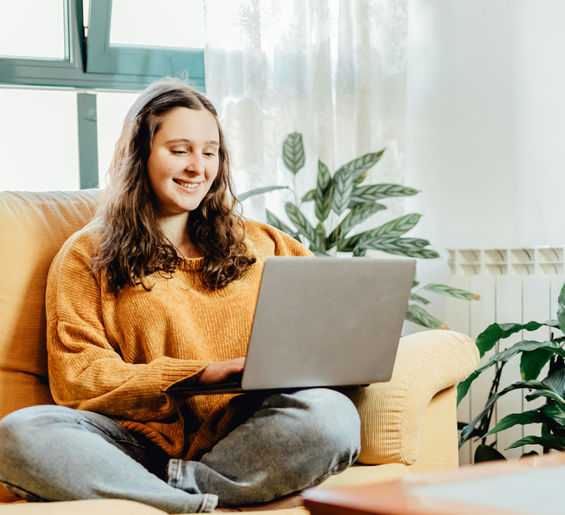 En kvinna sitter i en soffa med en bärbar dator